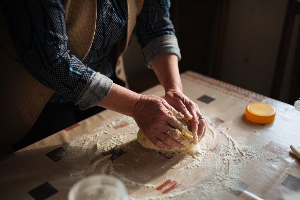 Floured hands kneading a ball of bread dough on a wooden table